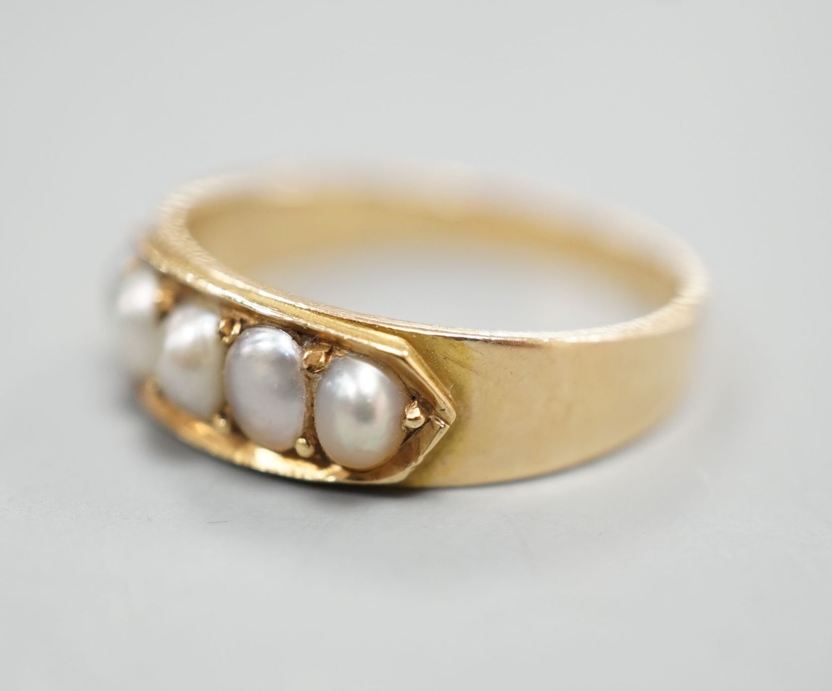 A yellow metal and graduated five stone split pearl set half hoop ring, size M, gross 3 grams.